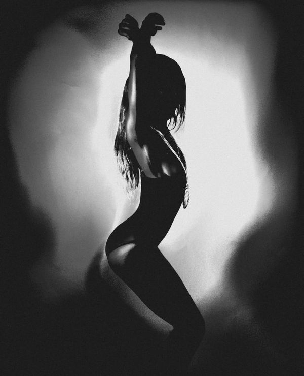 Black and white silhouette of a woman with arms raised, backlit in a pool of light.